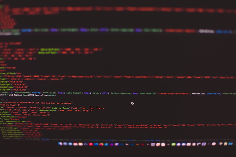 A close-up view of a computer screen displaying lines of colorful programming code in red, green, blue, and purple on a black background. The screen's edges show a blurred browser window with various